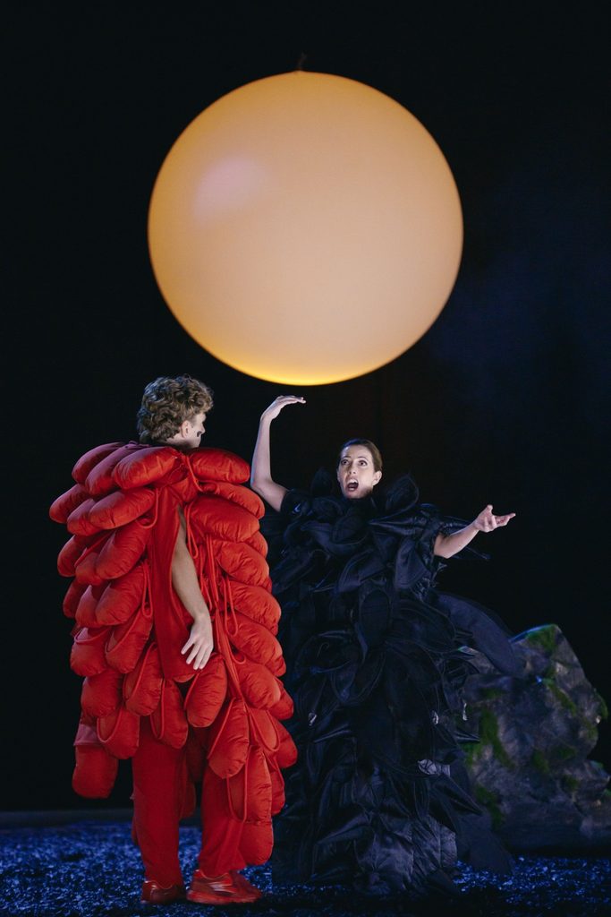 Two performers in red and black beneath the luminous sphere.