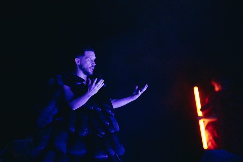 A performer in blue light with red glowing tubes behind him.
