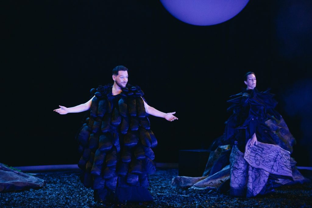Two performers in dark costumes lit blue on the Phaethon stage.