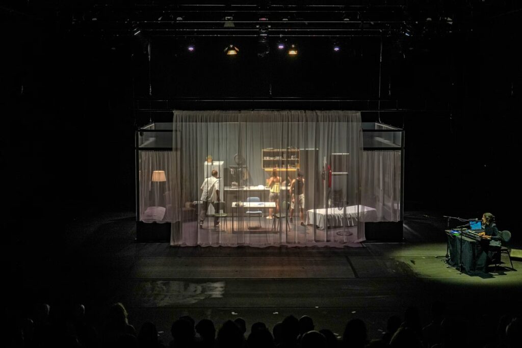 The full stage seen through translucent curtains, with the live musician at the side.